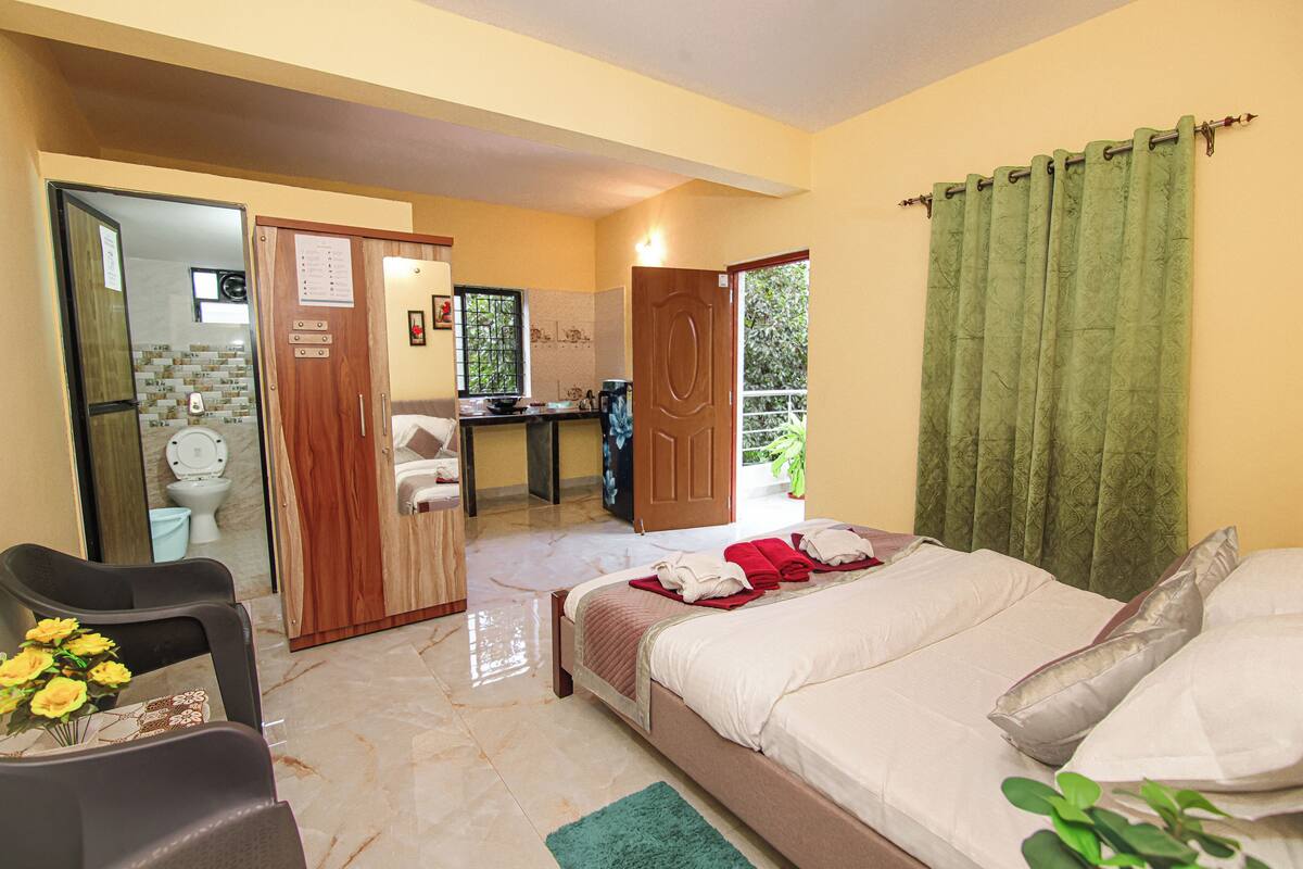 Une chambre d’hôtel avec un lit, un bureau, une chaise et une salle de bain visible à travers une porte ouverte.