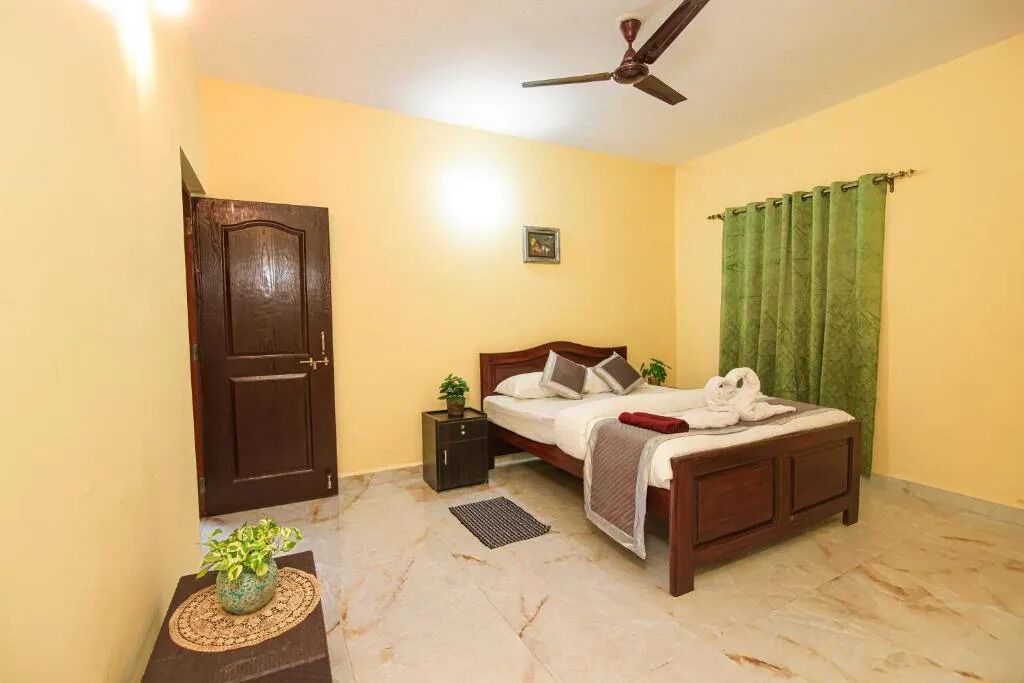 A bedroom with a bed, a nightstand, a ceiling fan, a door, and a green curtain.