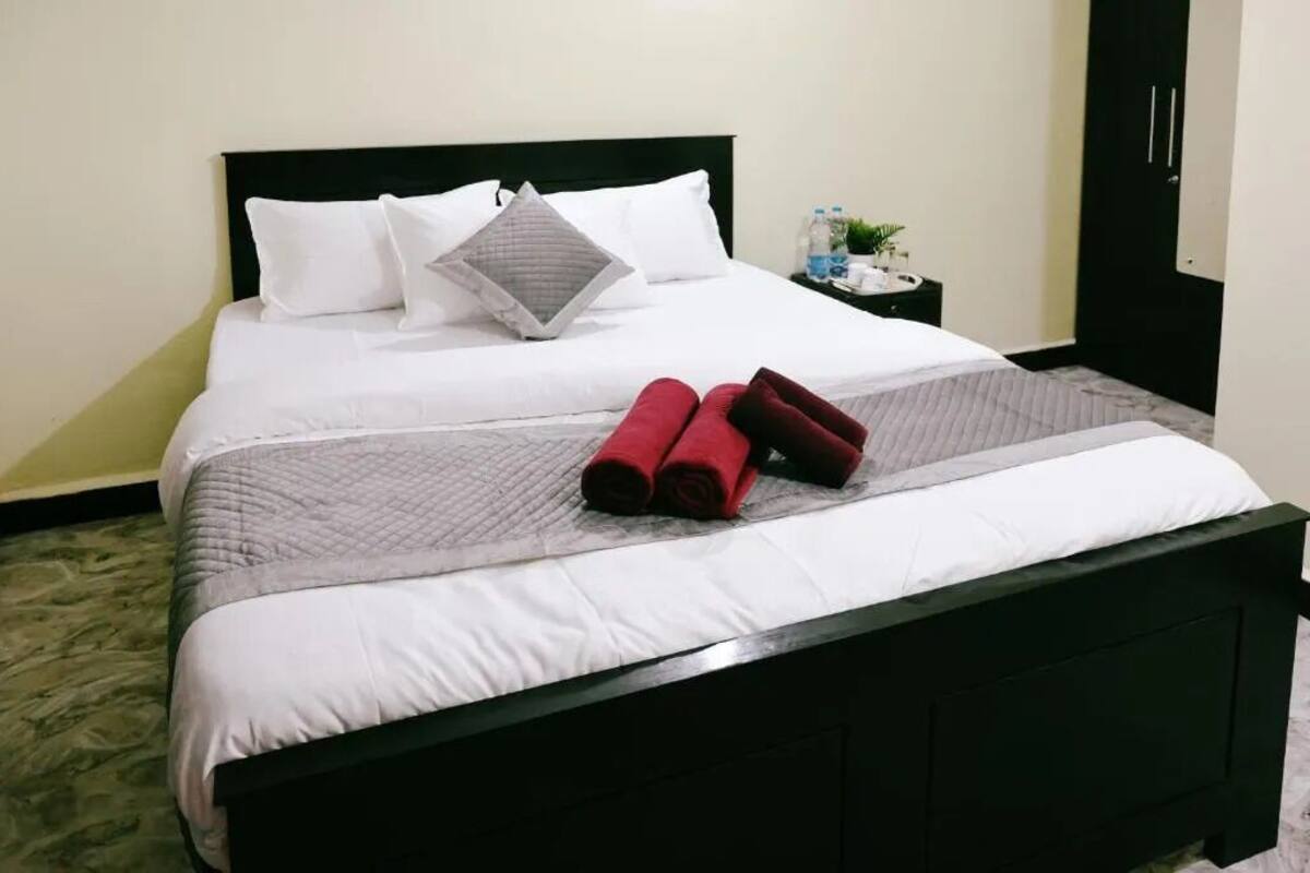 Un lit bien fait, avec des draps blancs, une couverture grise et deux oreillers rouges.