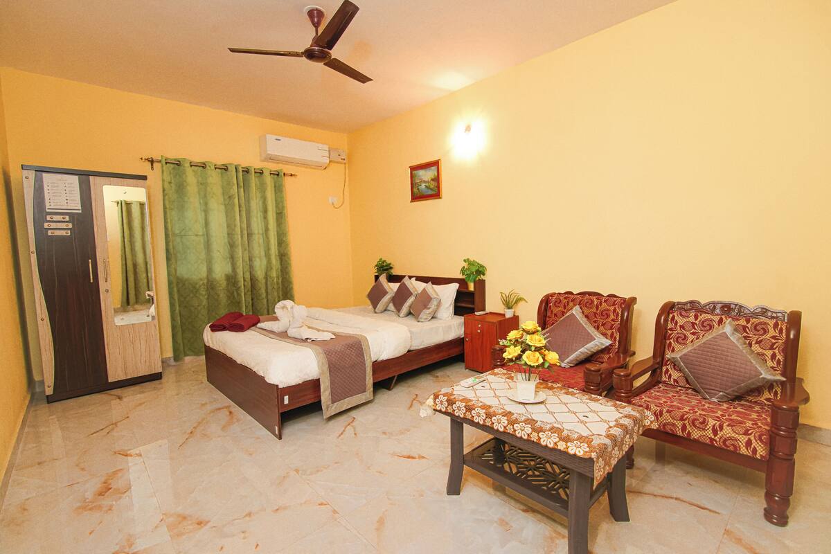 Une chambre d’hôtel avec un lit, deux chaises, une table, un ventilateur de plafond, une armoire et un rideau vert.