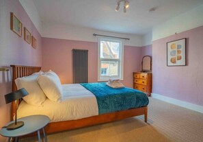 A bedroom with a bed, bedside table, dresser, window, and radiator.