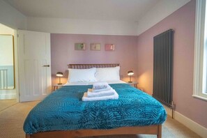 A bedroom with a bed, two bedside lamps, a radiator, and a door to another room. - Cute Cosy Cottage | Ramsgate Historic Area | 2bd (Kent)