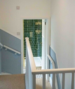 A staircase leading to a bathroom with green tiles, a shower, and a bathtub.