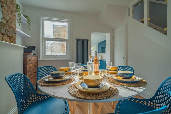 A dining room with a round table set for four, blue chairs, and a view of the city through a window.