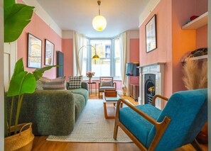 A cozy living room with a sofa, armchairs, a fireplace, and a large window. - Cute Cosy Cottage | Ramsgate Historic Area | 2bd (Kent)