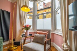 A cozy room with a chair, a floor lamp, and a vase of flowers. - Cute Cosy Cottage | Ramsgate Historic Area | 2bd (Kent)