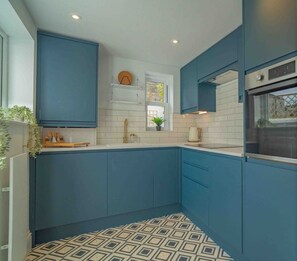 A modern kitchen with blue cabinets, white countertops, and a patterned floor. - Cute Cosy Cottage | Ramsgate Historic Area | 2bd (Kent)