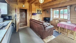 A cozy cabin interior with a wooden interior, a brown leather sofa, a dining table with a checkered tablecloth, a television, and a kitchen area with a microwave. - 1 bedroom accommodation in Berrow, near Malvern (Berrow, near Malvern)