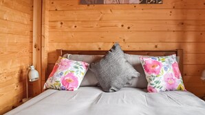 A wooden room with a bed, two pillows, a nightstand, and a wall-mounted lamp. - 1 bedroom accommodation in Berrow, near Malvern (Berrow, near Malvern)
