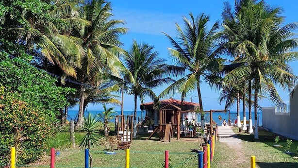 A beachside area with palm trees, a wooden structure, and a fenced play area. - House on the Island of Itaparica Bahia, with swimming pool and complete gourmet space (VERA CRUZ)