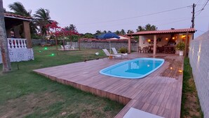 A backyard with a swimming pool, wooden deck, outdoor seating area, and a stone wall. - House on the Island of Itaparica Bahia, with swimming pool and complete gourmet space (VERA CRUZ)