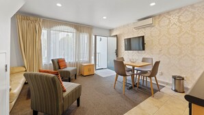 Ein modernes Wohnzimmer mit Sofa, Sessel, Esstisch und Stühlen. Ein Fernseher ist an der Wand befestigt und es gibt ein Fenster mit Vorhängen.