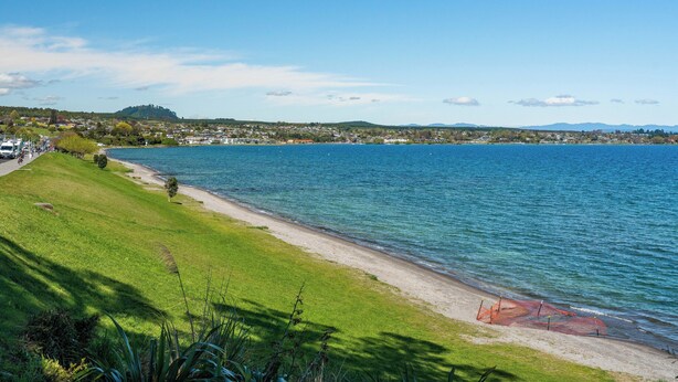 Blick auf einen See mit einer grünen Wiese, einem Sandstrand und einer Bootsanlegestelle.