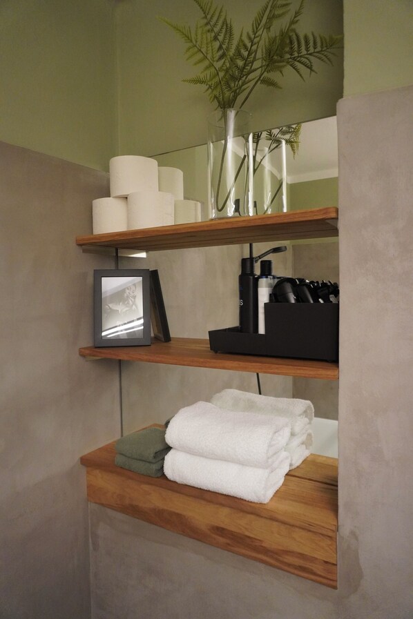 A bathroom with wooden shelves holding towels, toiletries, and a framed picture.