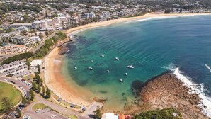 Une vue aérienne d’une zone côtière avec une plage, des eaux cristallines et plusieurs bateaux.