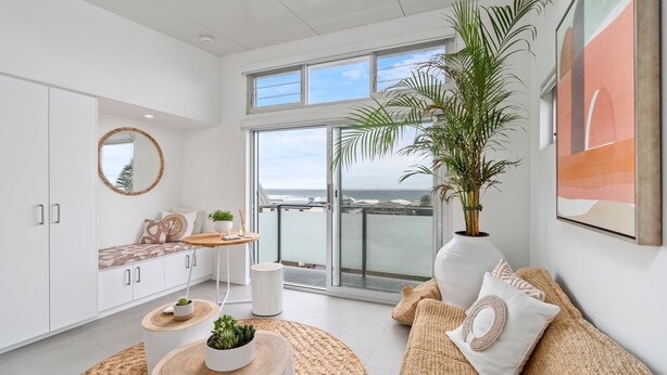 Un salon moderne avec vue sur l’océan, comprenant un canapé, une table ronde en bois et une grande plante en pot.