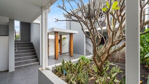 Une maison moderne avec un escalier menant à un espace extérieur couvert, un arbre et diverses plantes.