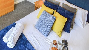 A neatly made bed with a blue headboard, multiple pillows in yellow and blue, a white blanket, and a rolled towel on a blue bedspread. - 2 bedroom accommodation in Lincoln (Lincoln)