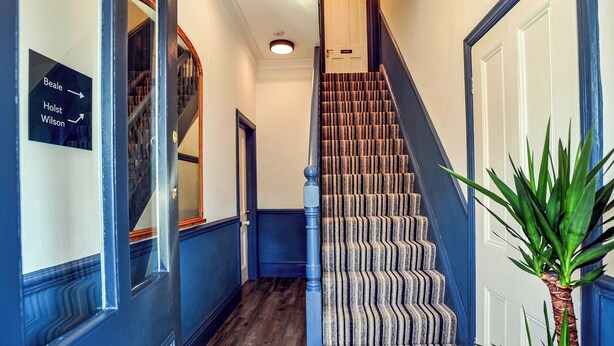 Una escalera con alfombra a rayas que lleva a una puerta con la leyenda 'Beale'.