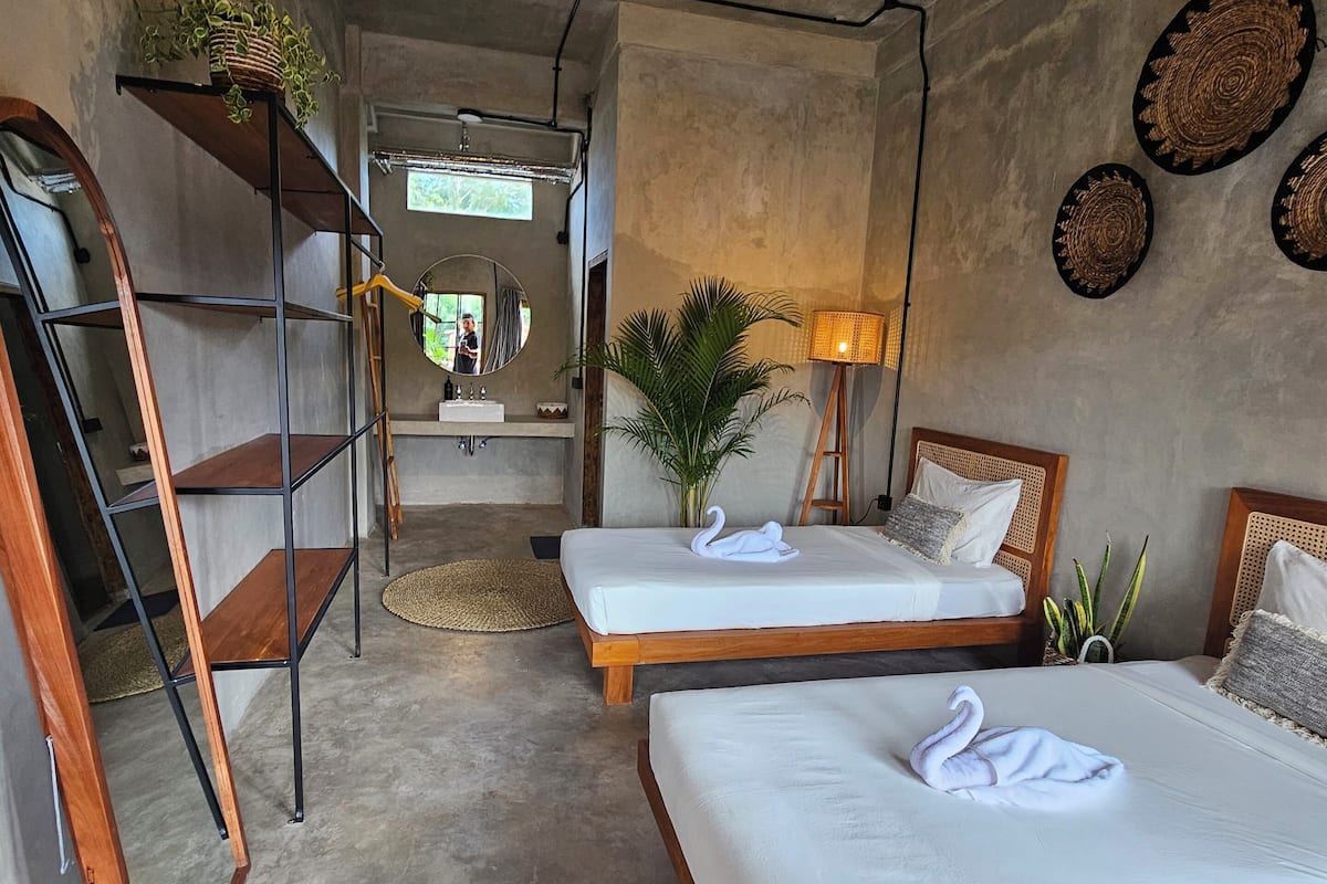 Habitación de hotel con dos camas, una escalera de madera, un espejo, una lámpara y vistas al exterior.
