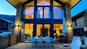 Una casa moderna de madera con un amplio balcón, mobiliario exterior y vistas del paisaje circundante.