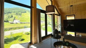 Una sala de estar moderna con ventanas amplias, un televisor de pantalla plana y techo de madera.