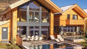 Una cabaña de madera moderna con balcón acristalado y zona de piscina.