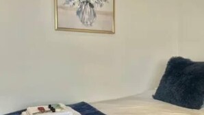 A neatly made bed with a dark blue cover, a framed floral artwork on the wall, and a dark grey pillow. - Leeds Urban Retreat- Pet Friendly Flat (Leeds)