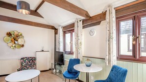 A room with a wooden ceiling, a round table, two blue chairs, a TV, and a wall clock.