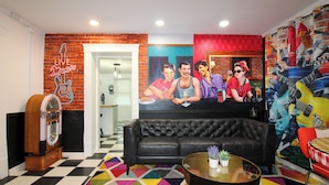 Una habitación con un sofá de cuero negro, una alfombra geométrica colorida, un jukebox antiguo y un mural de músicos.