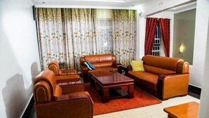A living room with leather sofas, a wooden coffee table, and curtains. - The Vibrant Loadge (Kigali)
