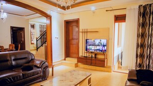 A living room with a brown leather sofa, a marble coffee table, and a television displaying a program. - The Vibrant Loadge (Kigali)