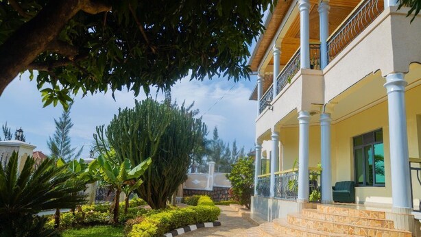 A building with a covered porch, a stone pathway, and a variety of greenery including trees and shrubs. - The Vibrant Loadge (Kigali)