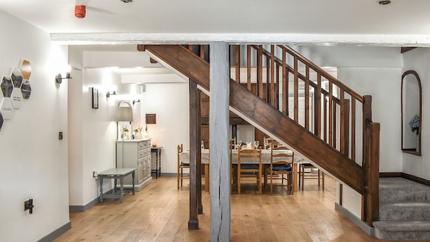 Una habitación amplia con una escalera de madera, un comedor y una cocina visible al fondo.