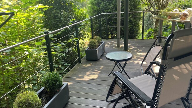 Una terraza de madera con barandilla metálica, una pequeña mesa redonda y dos sillas.