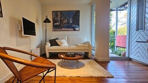 Una sala de estar con un sofá, una silla de madera, una mesita de centro, un televisor y un cuadro.