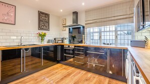 Une cuisine moderne avec un plan de travail en bois, des meubles de couleur noire et une vue sur l’extérieur.
