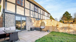 Une maison avec une façade en pierre, une terrasse en bois, du mobilier d’extérieur et un fauteuil suspendu.