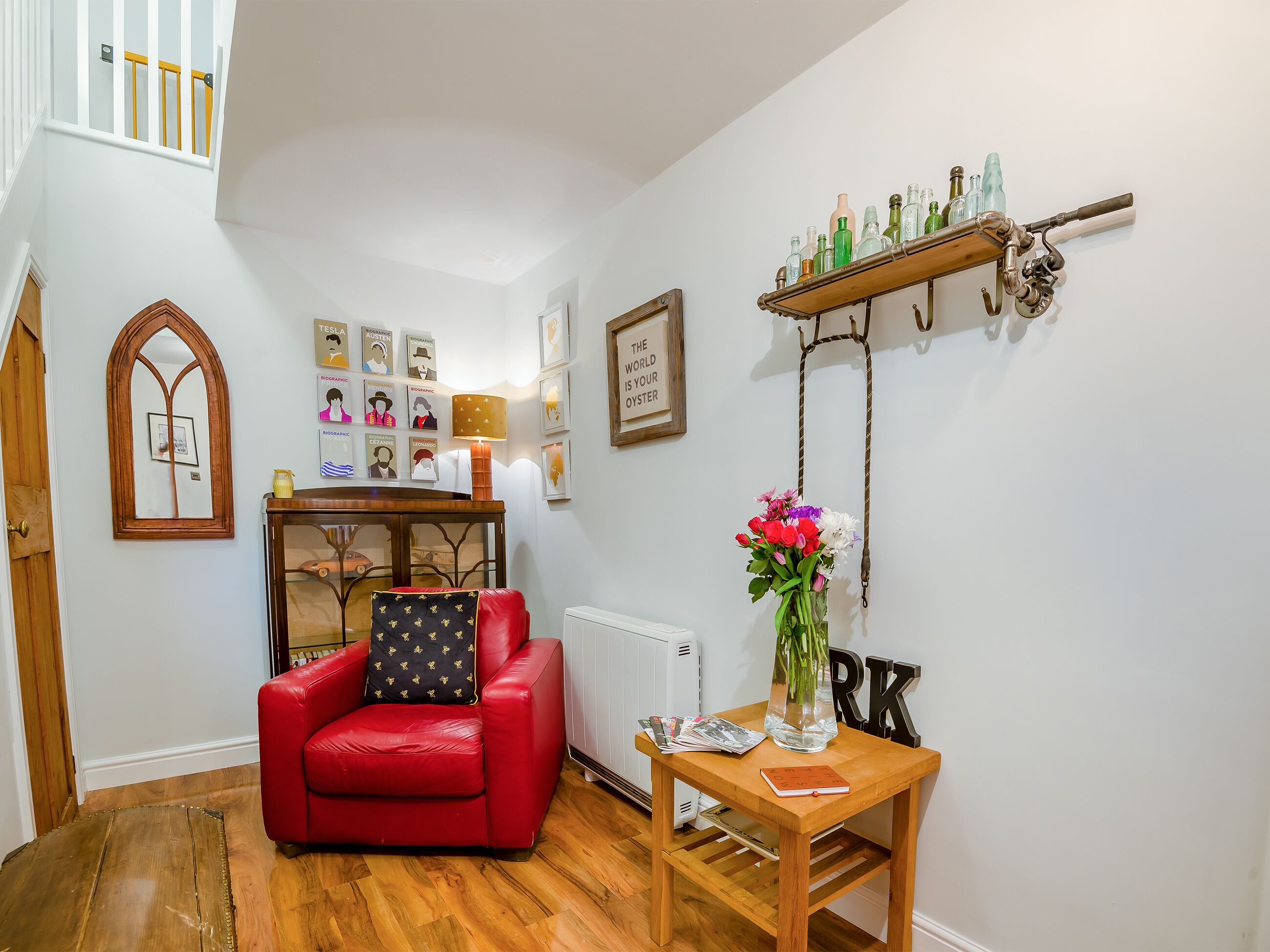 A red leather chair, a wooden table with a vase of flowers, and a wall-mounted shelf with bottles.
