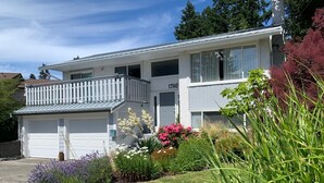 A two-story house with a white exterior, a garage, and a balcony. - Traveller's Sanctuary in Supernatural BC. for the Outdoor Enthusiast (Comox)