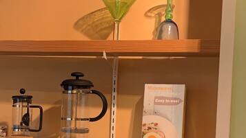 Uma prateleira com uma cafeteira, um copo de vidro verde e a caixa de um cozinhador de ovos elétrico.