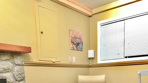 A cozy living room with a stone fireplace, a wooden coffee table with a floral-patterned table runner, a comfortable armchair with a patterned cushion, and a wooden dresser. - Traveller's Sanctuary in Supernatural BC. for the Outdoor Enthusiast (Comox)