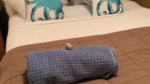 A bed with a brown quilted cover, two pillows with octopus designs, and a folded blue blanket with a gold button. - Traveller's Sanctuary in Supernatural BC. for the Outdoor Enthusiast (Comox)