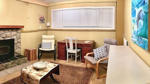 A cozy living room with a fireplace, a dining table, two chairs, a sofa, and a large window with blinds. - Traveller's Sanctuary in Supernatural BC. for the Outdoor Enthusiast (Comox)