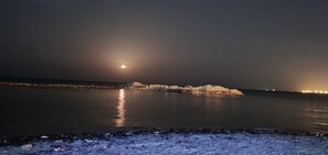 A nighttime coastal scene with calm waters reflecting the moon and distant lights. - SIESTA HOTEL  (Djibouti)