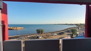 Μια θέα σε μια παραλία με καθαρό ουρανό, μια αμμώδη ακτή και σταθμευμένα αυτοκίνητα κατά μήκος της παραλιακής οδού.