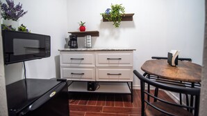 A compact kitchen with a microwave, a coffee maker, and a small table with a chair. There is a shelf with a plant and a strawberry on it. - Private Studio Suite (Lakeland)