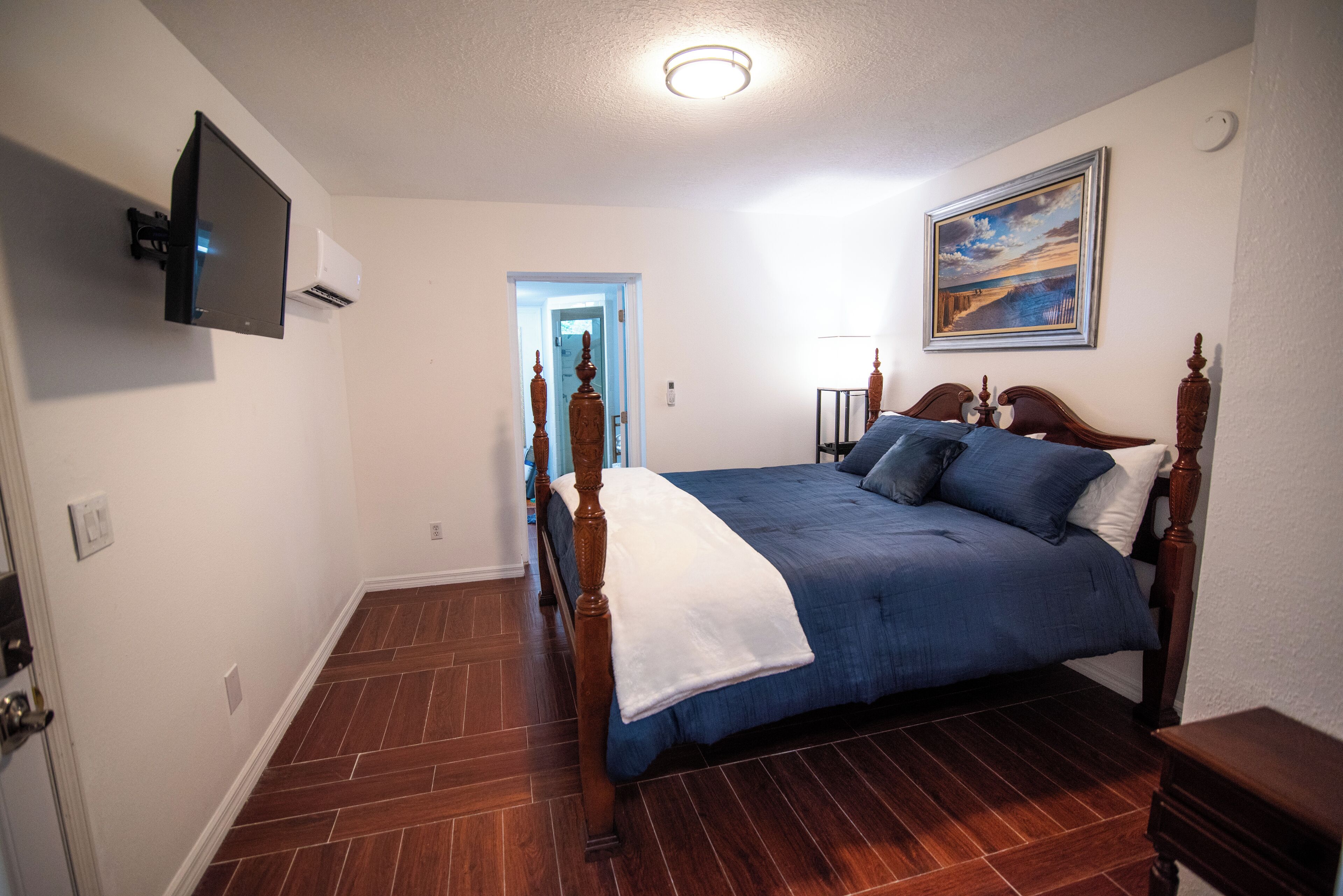 Ein Schlafzimmer mit einem hölzernen Bett, einem flachbildfernseher an der Wand und einem Gemälde über dem Bett.