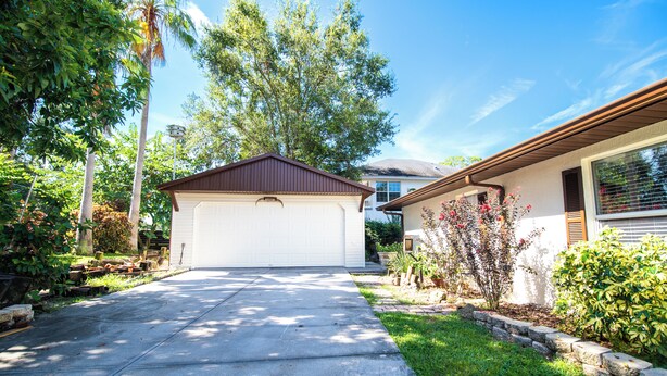 A residential driveway leading to a garage with a white garage door, surrounded by lush greenery and trees. - Private Studio Suite (Lakeland)