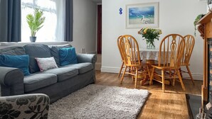 A living room with a grey sofa, blue cushions, a wooden dining table with chairs, a white rug, and a painting of seagulls on the wall. - 2 bedroom accommodation in Taff&rsquo;s Well, near Cardiff (Taff&rsquo;s Well, near Cardiff)